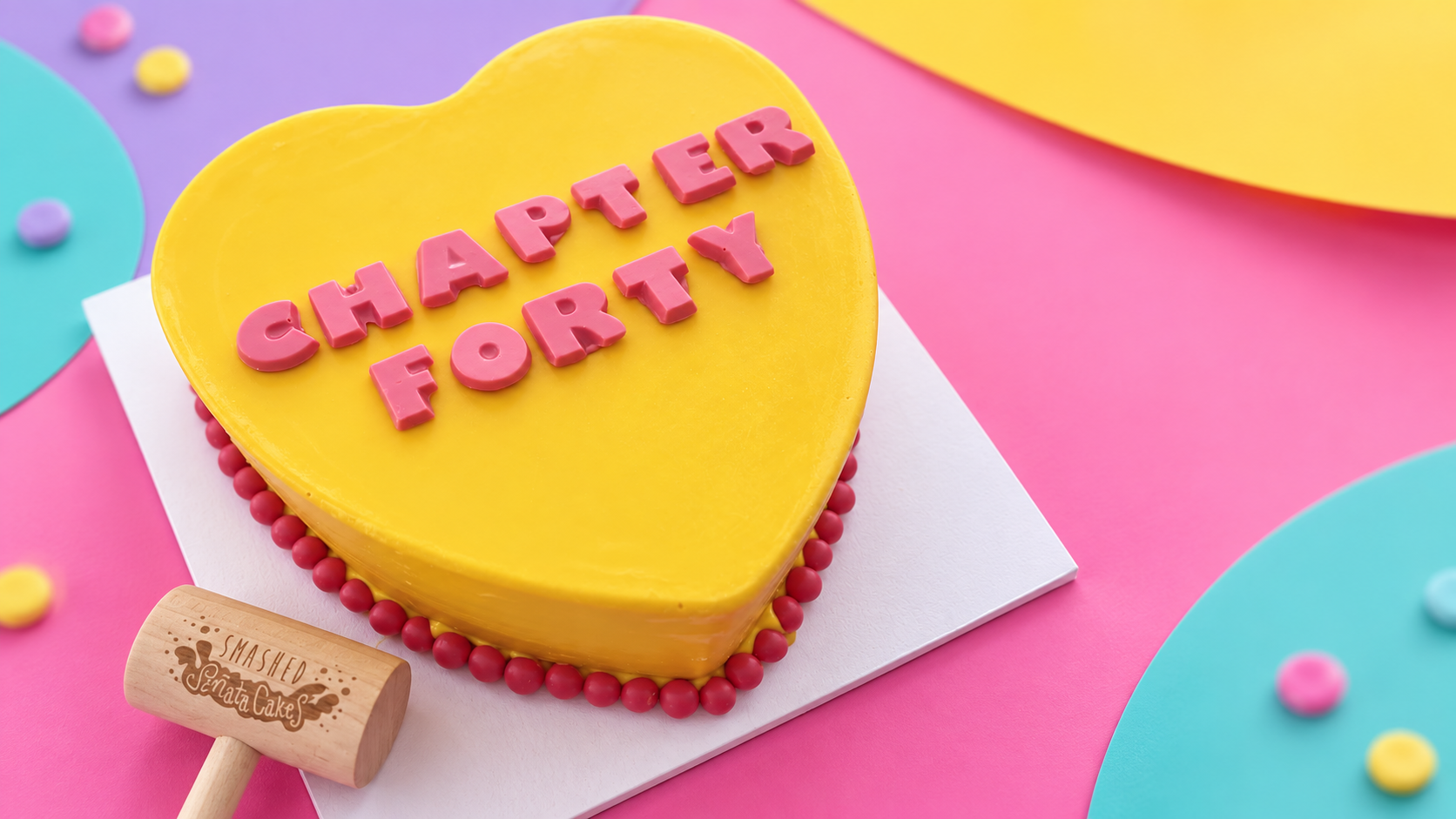 Yellow personalised Heartbreaker SmashCake with pink letters and branded wooden mallet on a colourful studio backdrop
